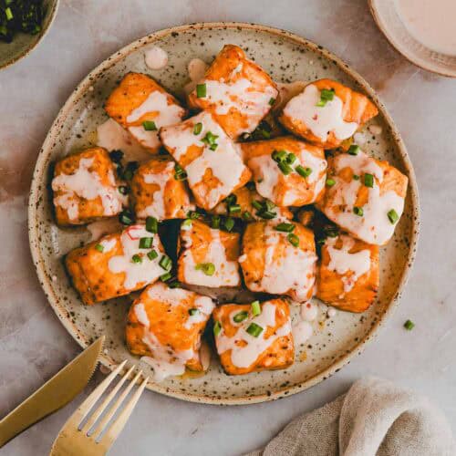 air fryer bang bang salmon on a plate drizzled with bang bang sauce and garnished with chopped scallions