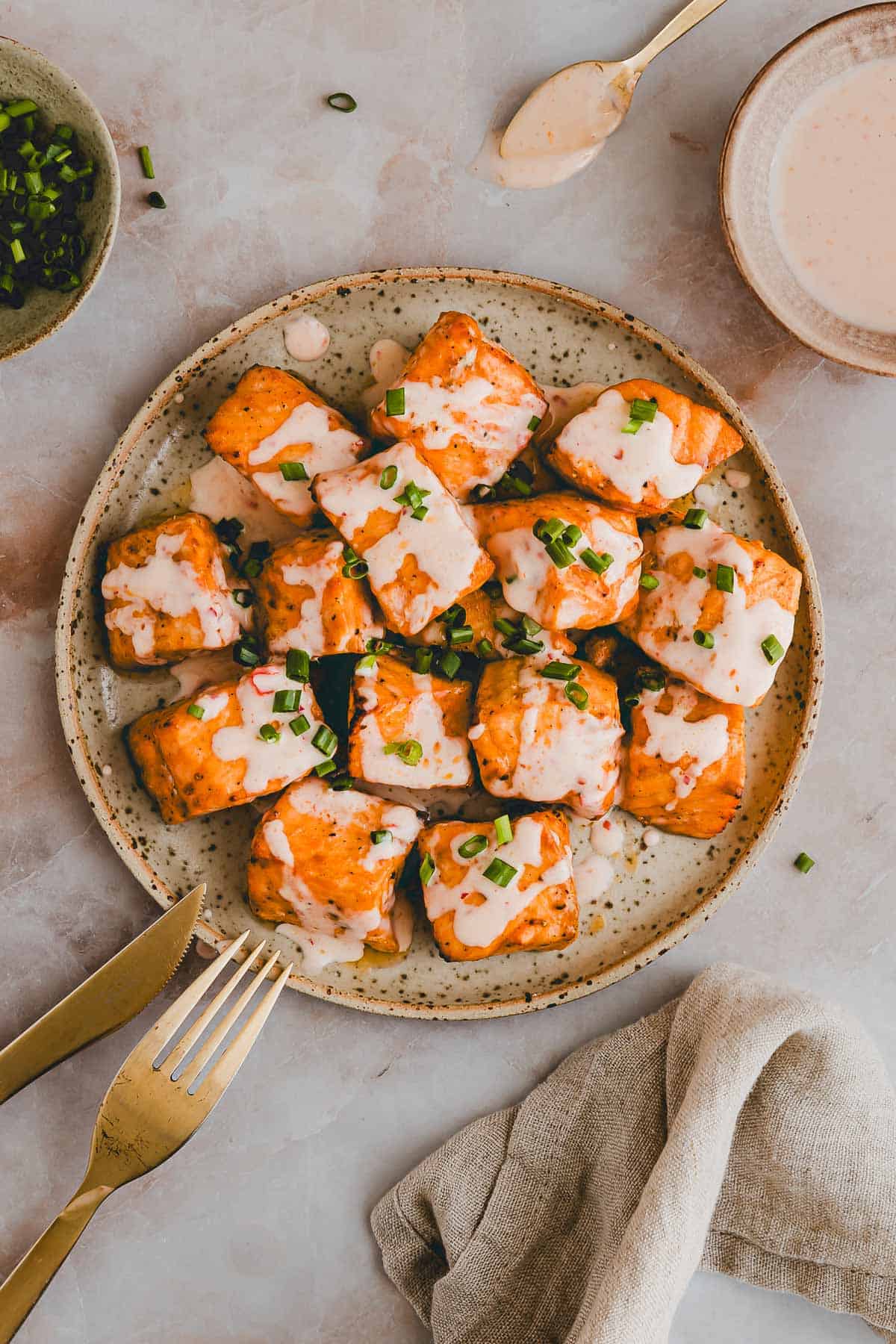 air fryer bang bang salmon bites on a plate drizzled with bang bang sauce and garnished with chopped scallions