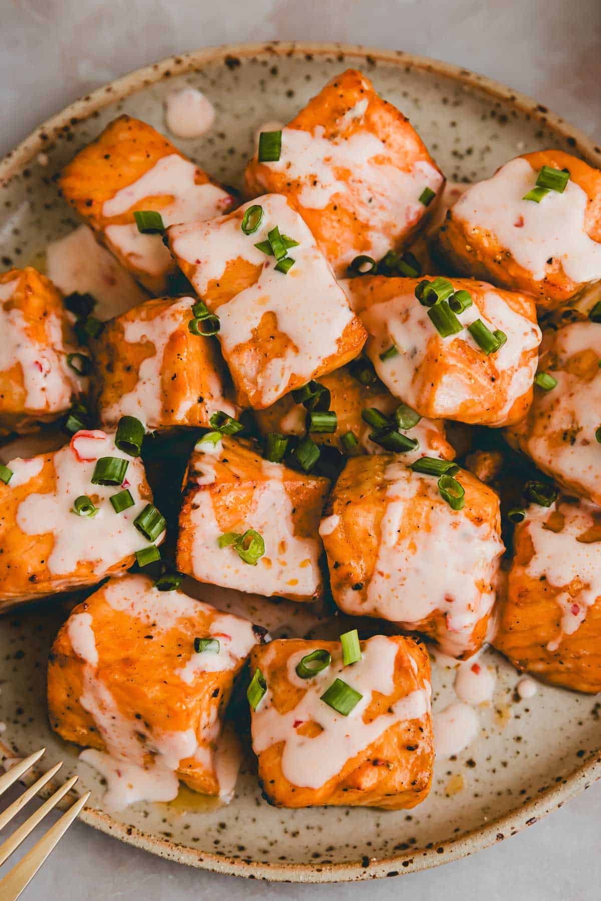 air fryer bang bang salmon bites on a plate drizzled with bang bang sauce and garnished with chopped scallions