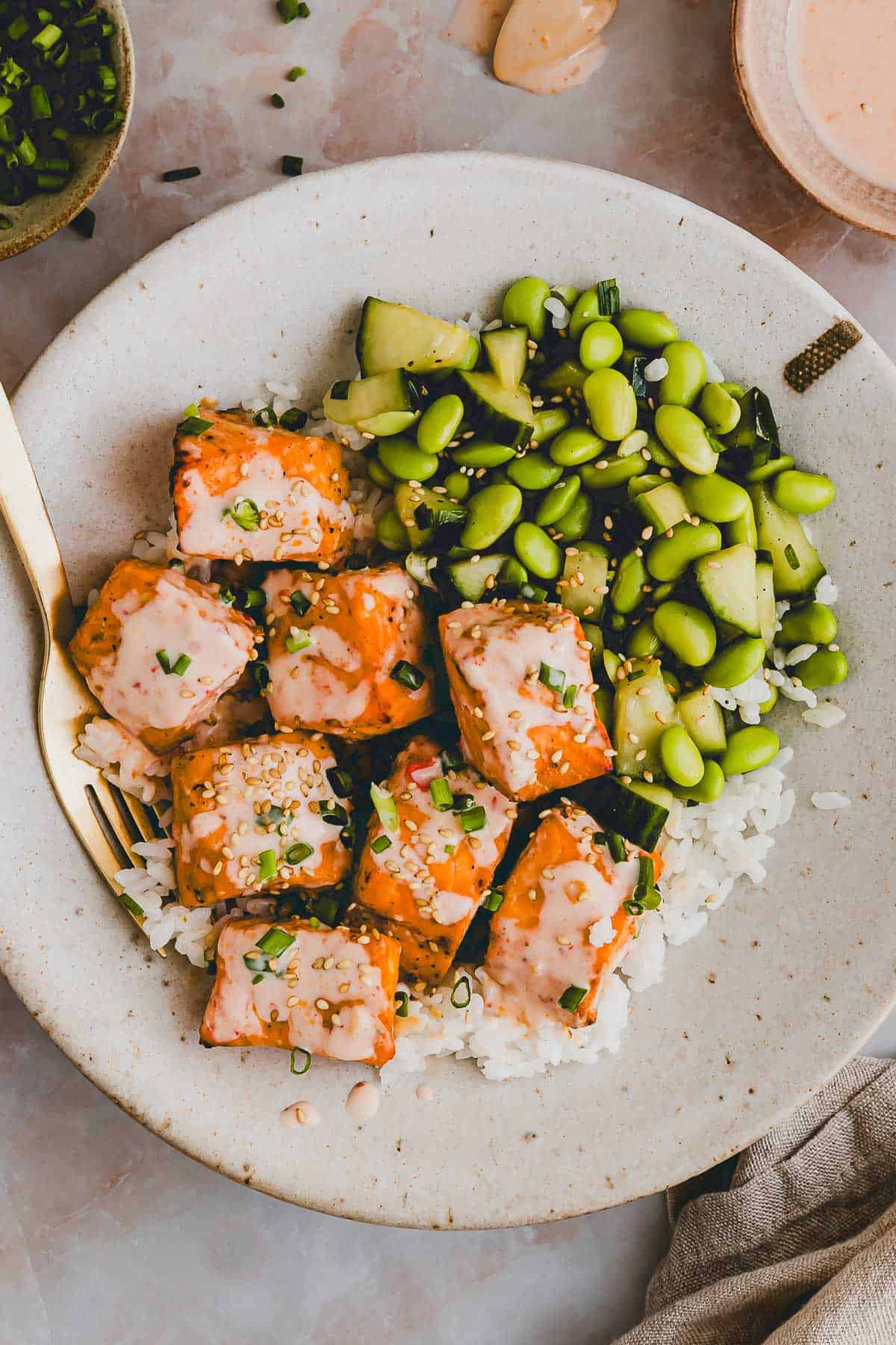 bang bang salmon bowl with cucumber edamame salad in a bowl with a golden fork